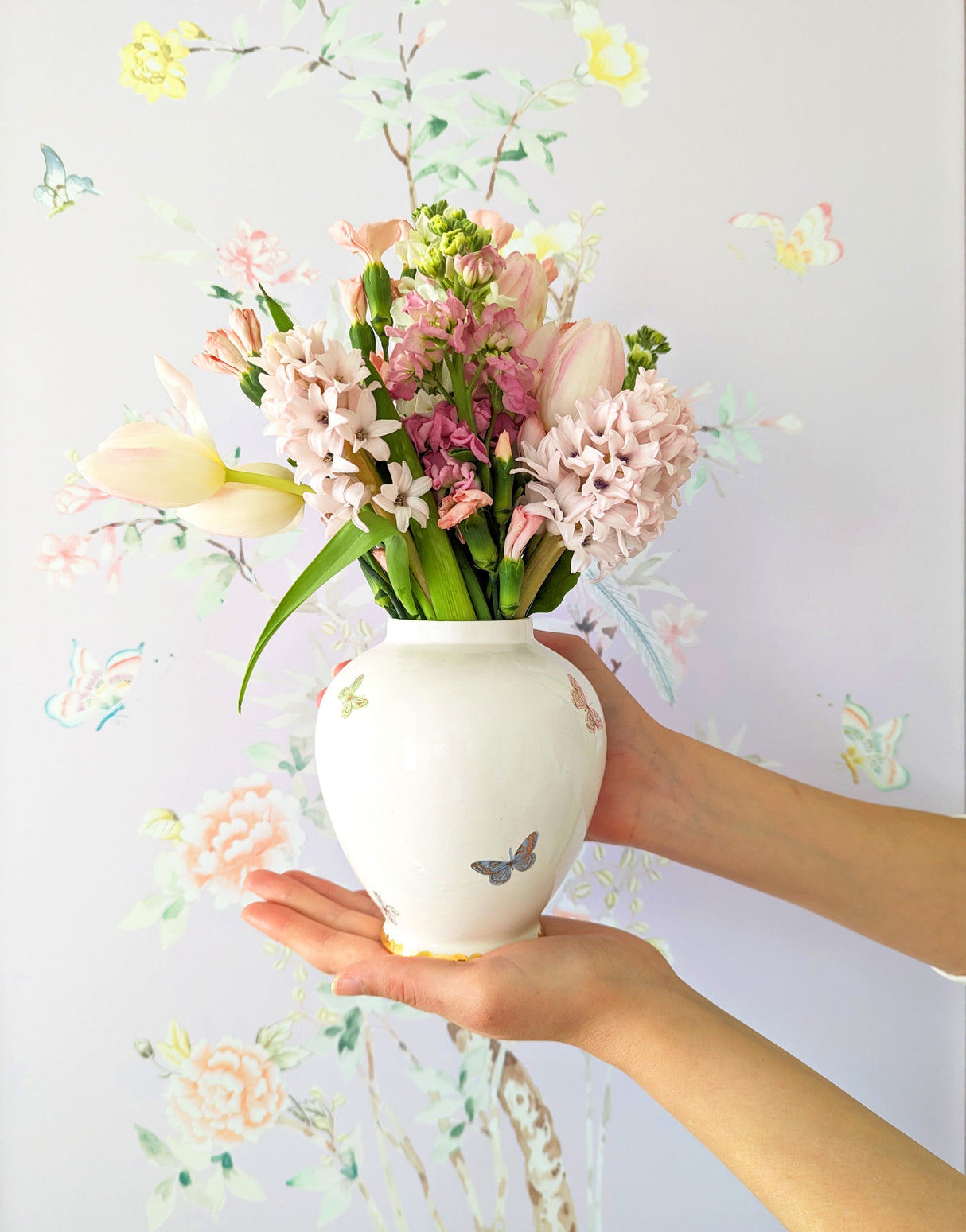 Fresh floral arrangement in a small white ginger jar with hand painted butterflies and gold details.