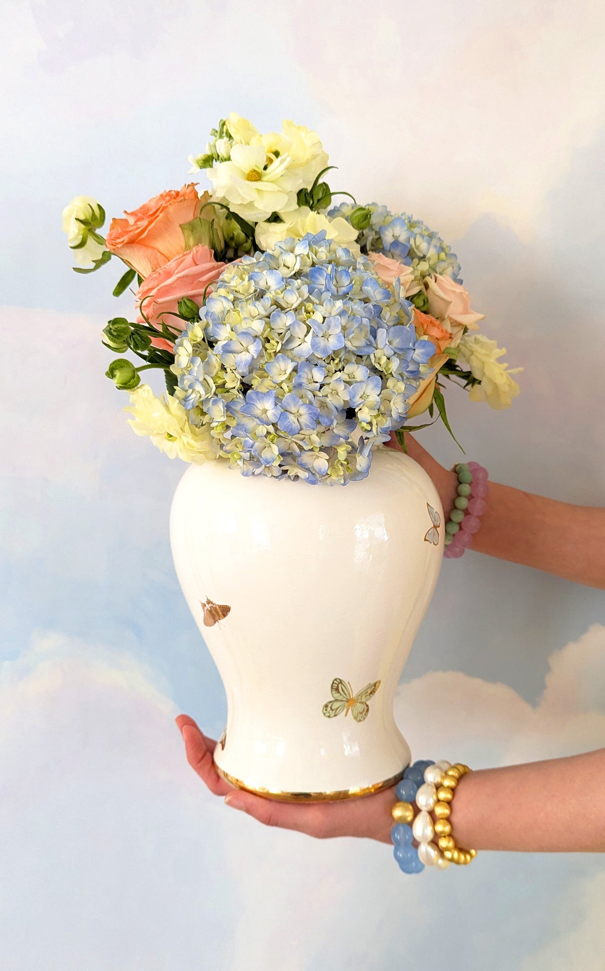 Fresh floral arrangement in a large white ginger jar with hand painted butterflies with gold details.